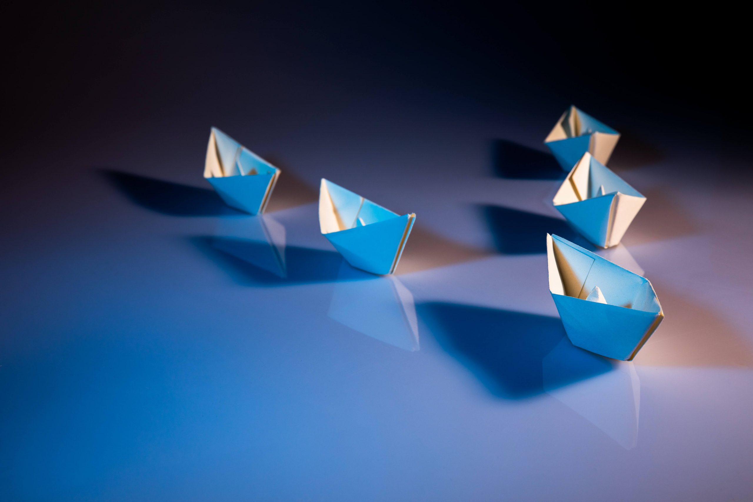 five paper boats moving towards the light